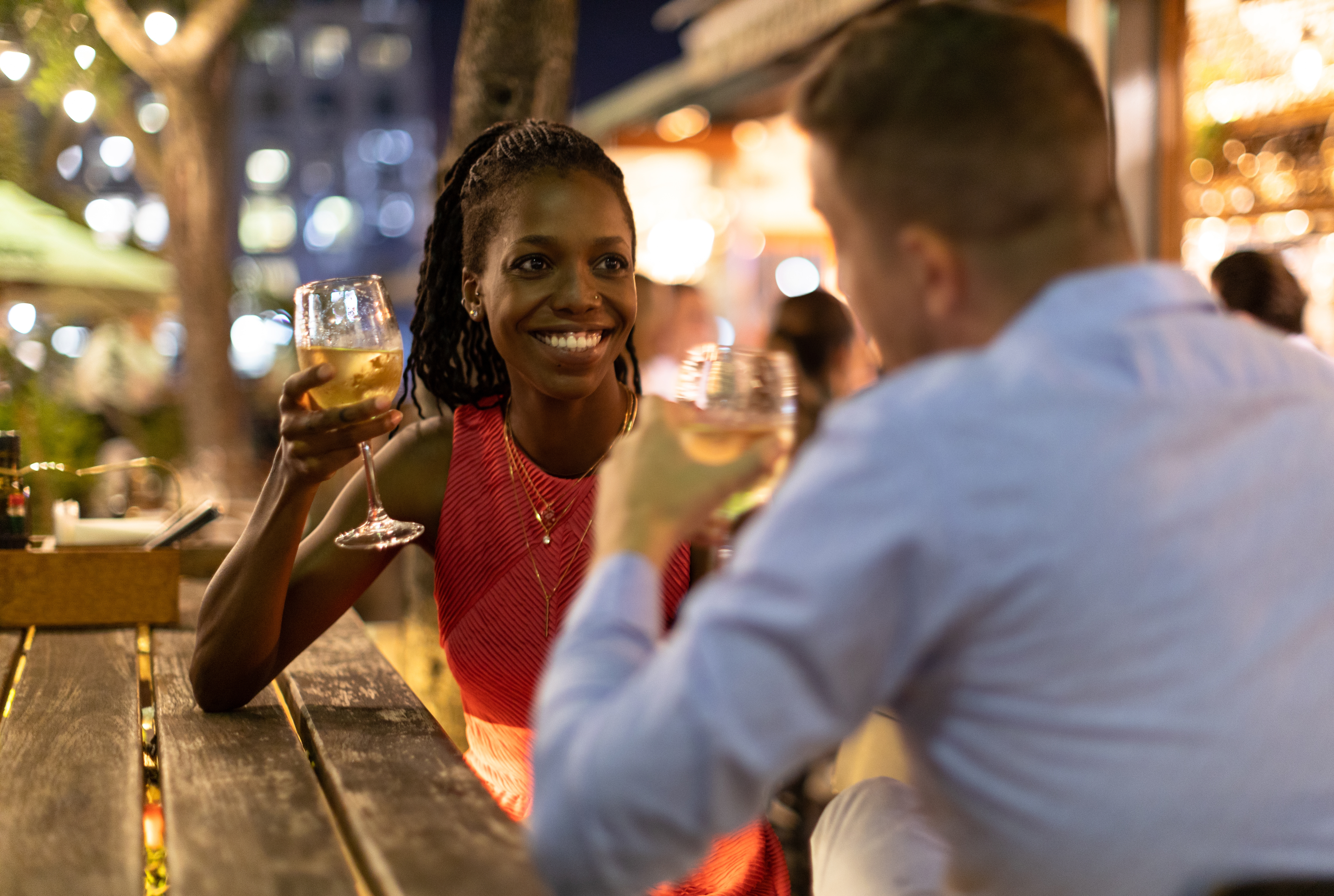 To personer nyter en uformell utendørsmiddag, deler en skål med vinglass, sittende ved et trebord i livlige omgivelser