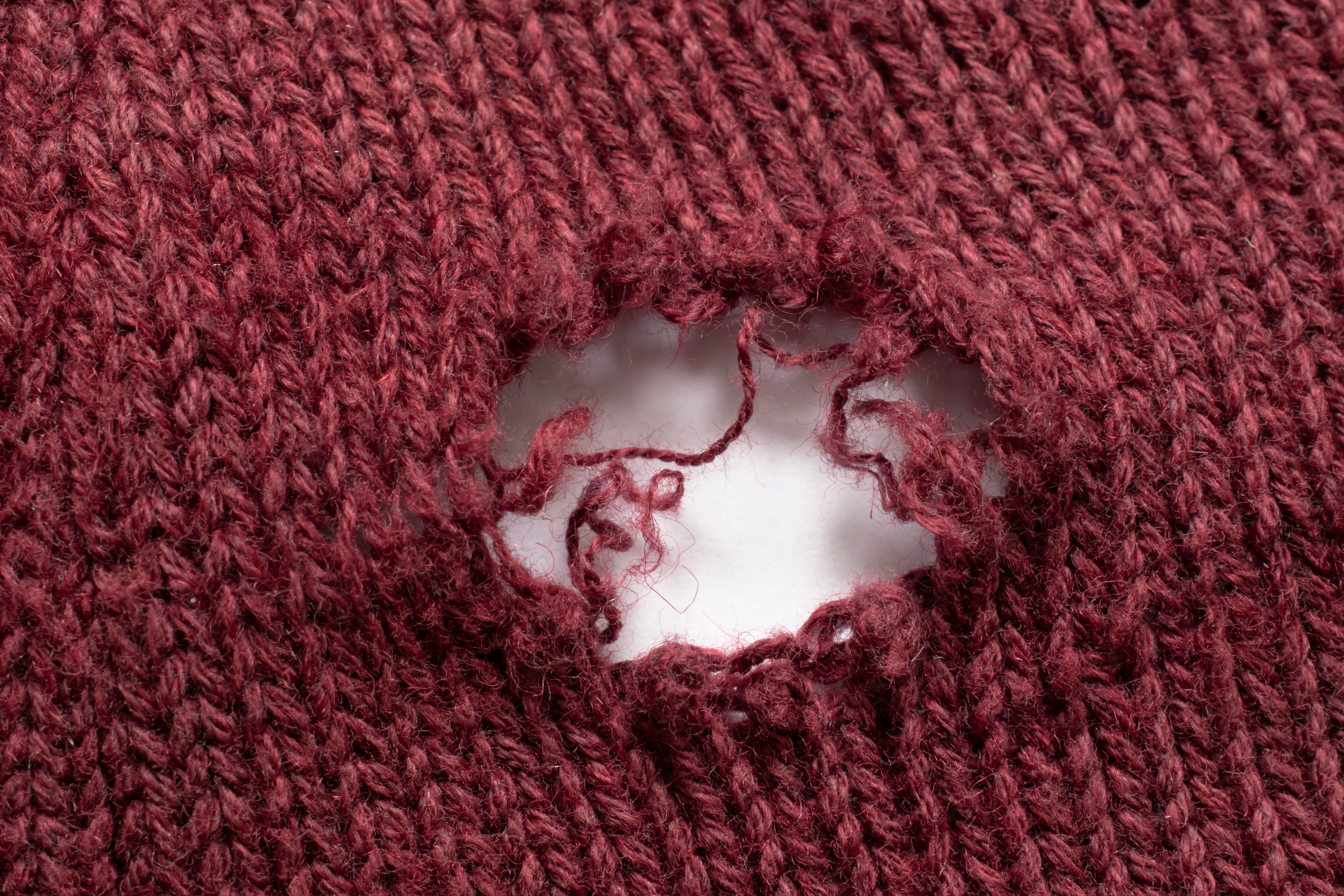 Et nærbilde av et strikket stoff med et stort hull, som viser opprevet garn og hvit bakgrunn under