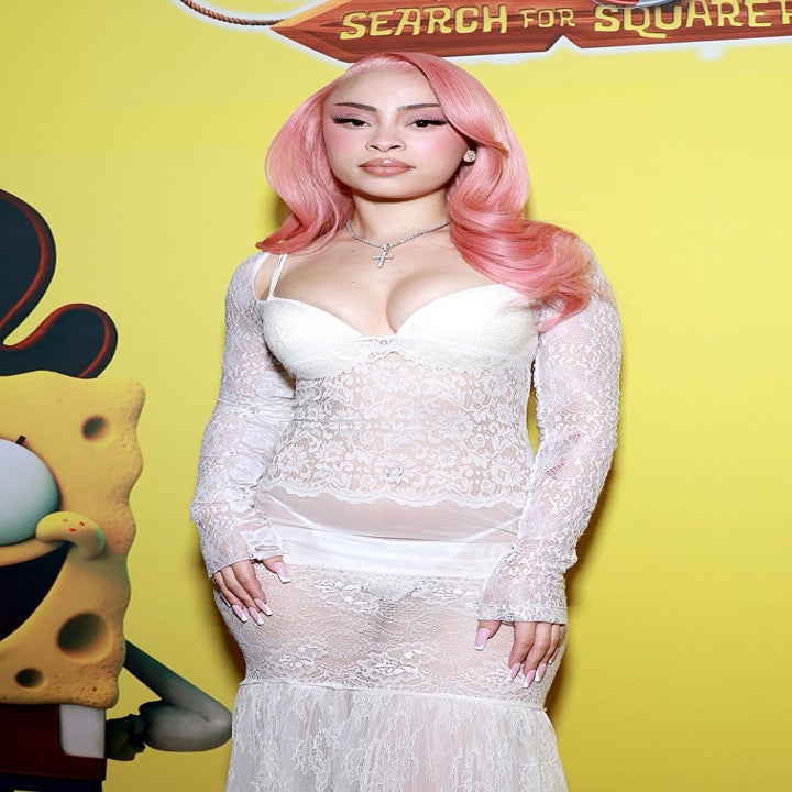 Person with pink hair in a lace dress poses beside an animated character on a yellow backdrop