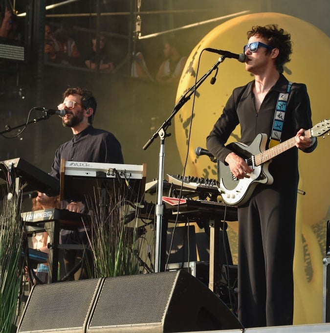 To musikere opptrer på scenen; den ene spiller keyboard, den andre gitar. Begge bruker solbriller. En stor ballongskulptur er synlig i bakgrunnen