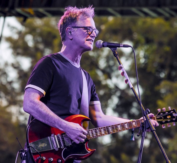 Musiker i uformelt antrekk spiller elektrisk gitar og synger på utendørsscenen under en liveopptreden