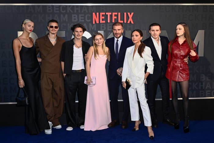 Group of radical   connected  a reddish  carpet, each  dressed elegantly; immoderate   successful  tailored suits, others successful  dresses. Netflix lawsuit   backdrop is visible