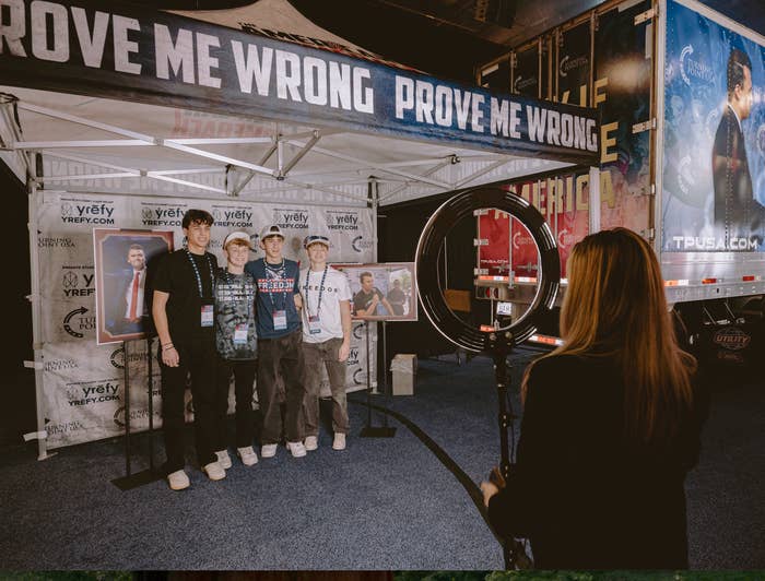 People airs  nether  a structure   with a "Prove Me Wrong" banner, portion    a idiosyncratic   photographs them utilizing a ringing  light