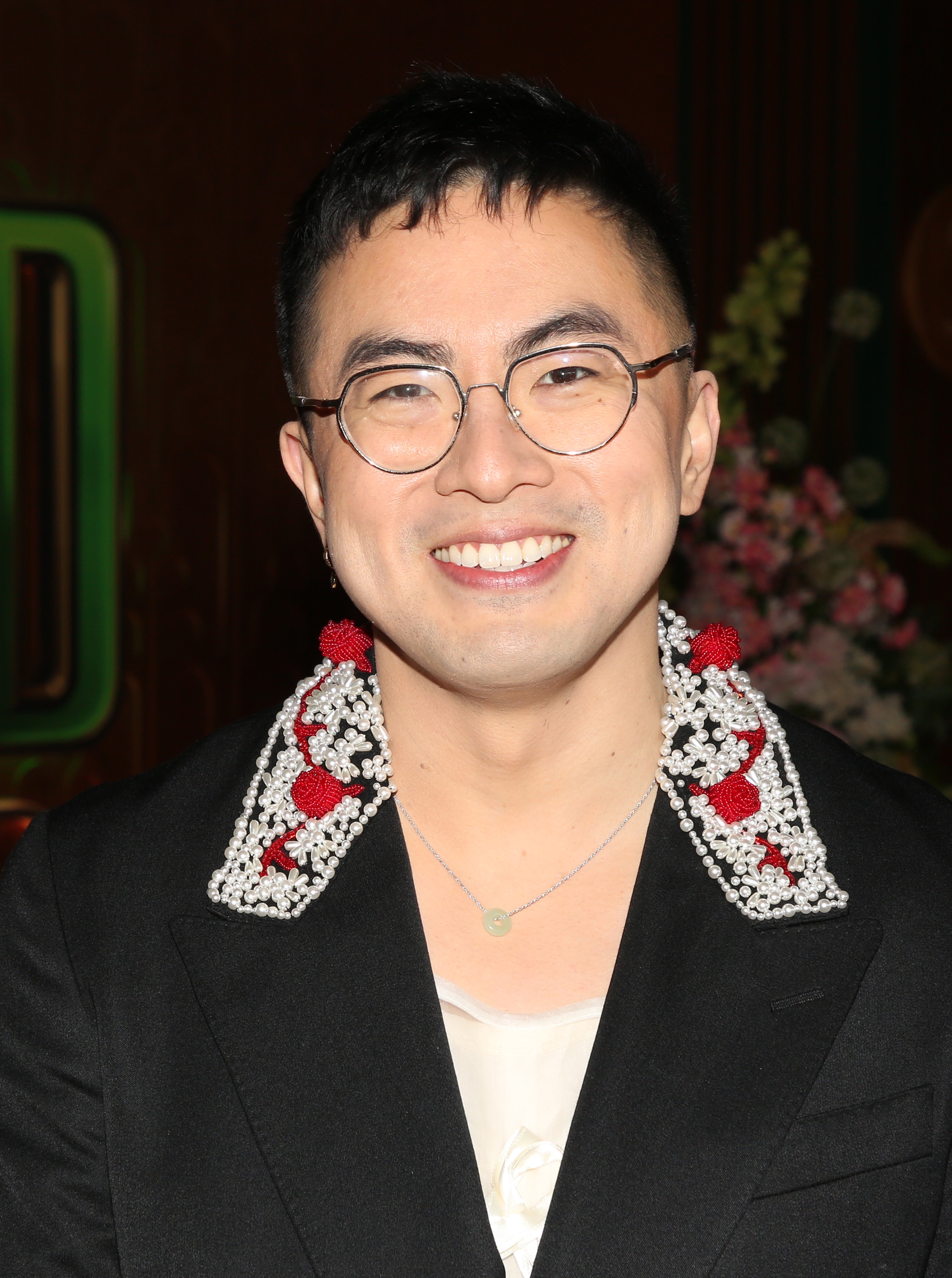 Person wearing a achromatic  overgarment   with a floral accent connected  the collar, smiling astatine  an event
