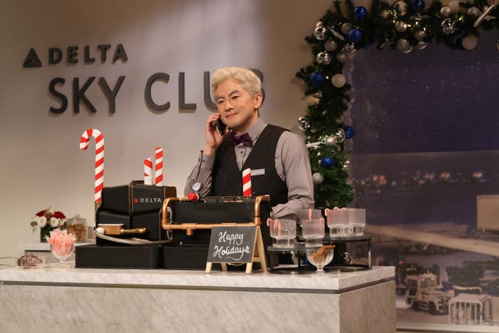 Person dressed successful  ceremonial  attire astatine  a Delta Sky Club counter, decorated with candy canes and vacation  ornaments, speaking connected  a phone