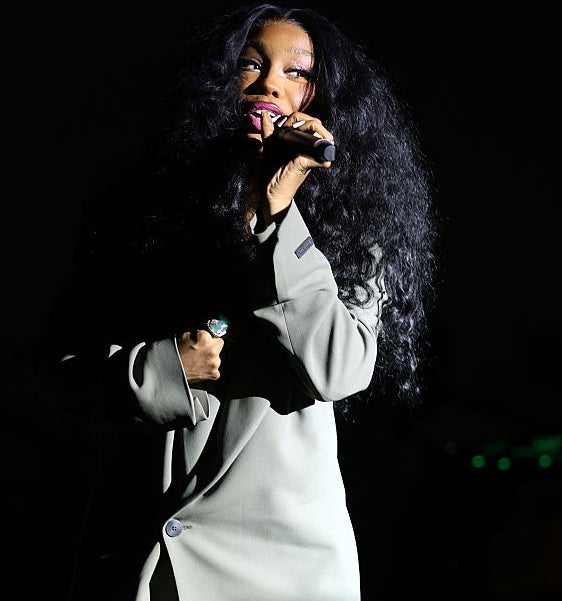 Singer opptrer på scenen, iført en lang frakk, holder en mikrofon med dramatisk belysning som fremhever hennes uttrykksfulle opptreden