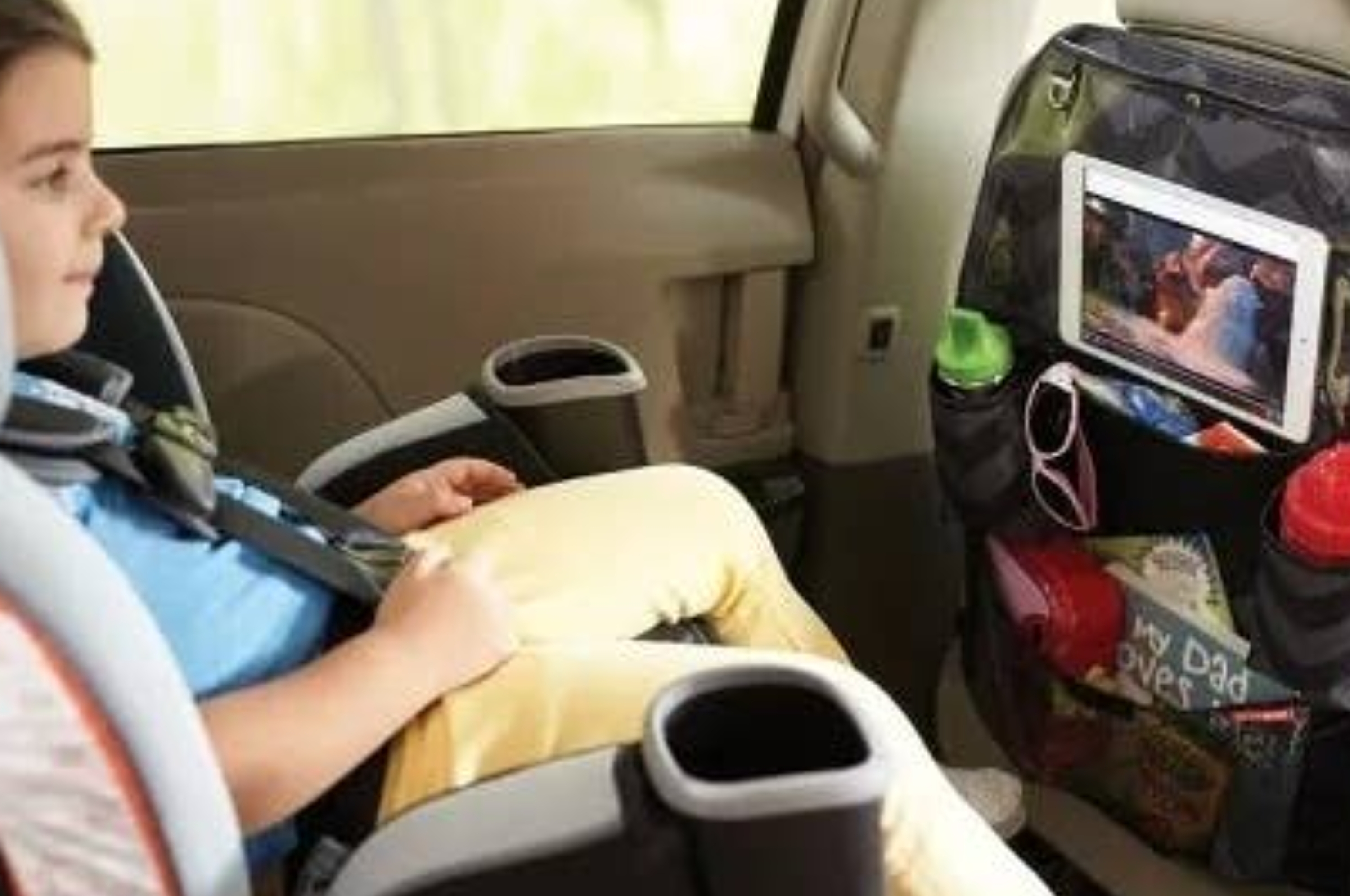 Child in a car seat watching a tablet on a car seat organizer with drinks and snacks in pockets