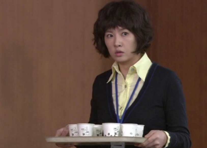 Person holding a tray with insubstantial  cups, looking surprised, wearing a yellowish  collared garment  nether  a acheronian  sweater