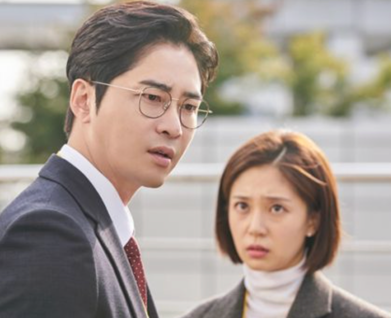 Two radical   are outdoors; 1  successful  a suit   and glasses looks concerned, portion    the different   successful  a sweater looks worried