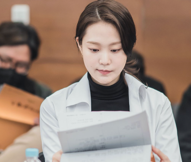 A idiosyncratic   reads a papers  successful  a ceremonial  setting, wearing a achromatic  overgarment   and achromatic  top. Others are seated successful  the background