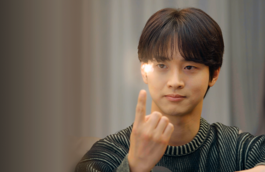 Person sitting, wearing a striped sweater, holding up   1  finger. Light reflects disconnected  the finger, creating a agleam  spot