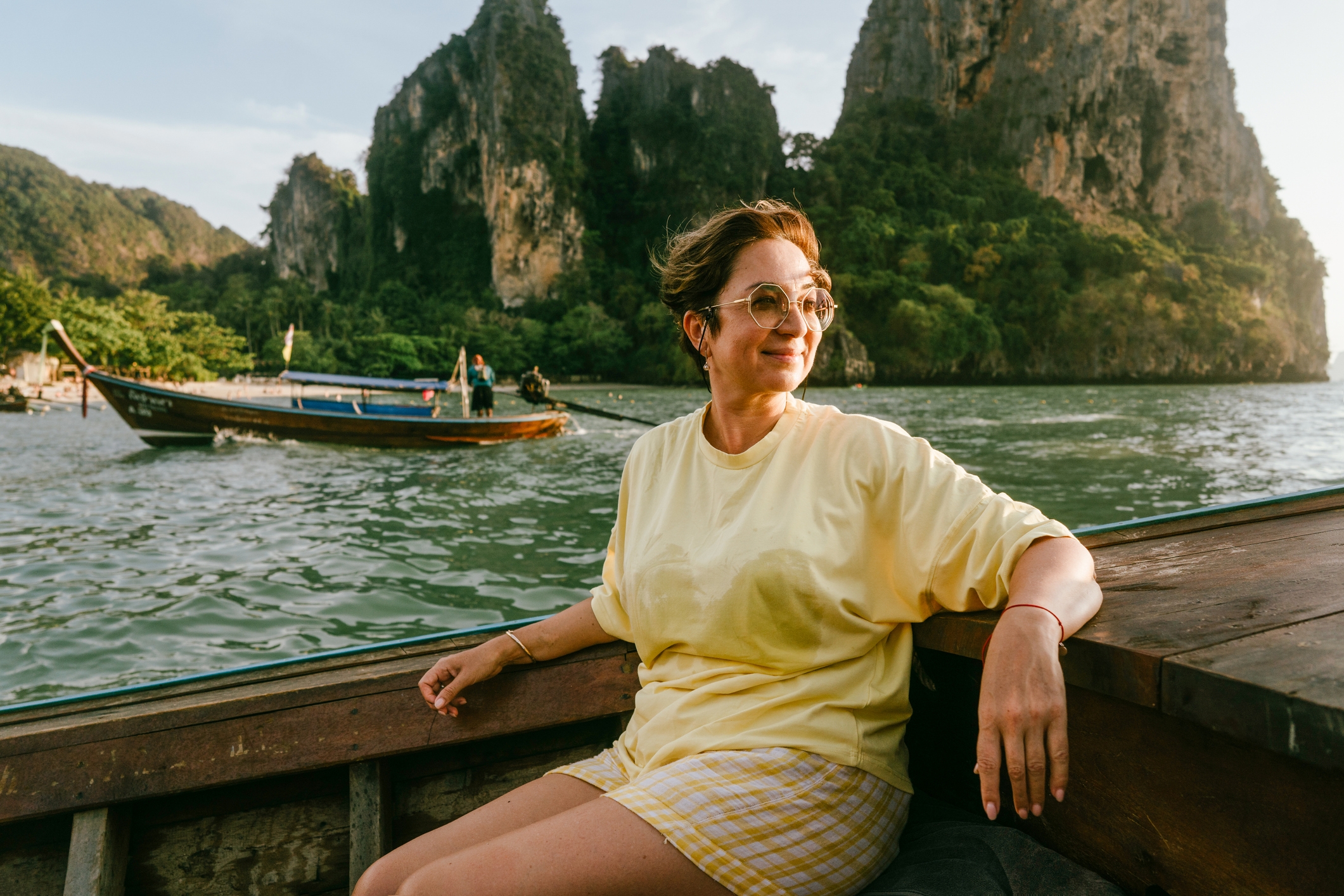 Person in casual clothes enjoying a boat ride on a serene river with limestone cliffs in the background. Sunglasses reflect the sunny setting
