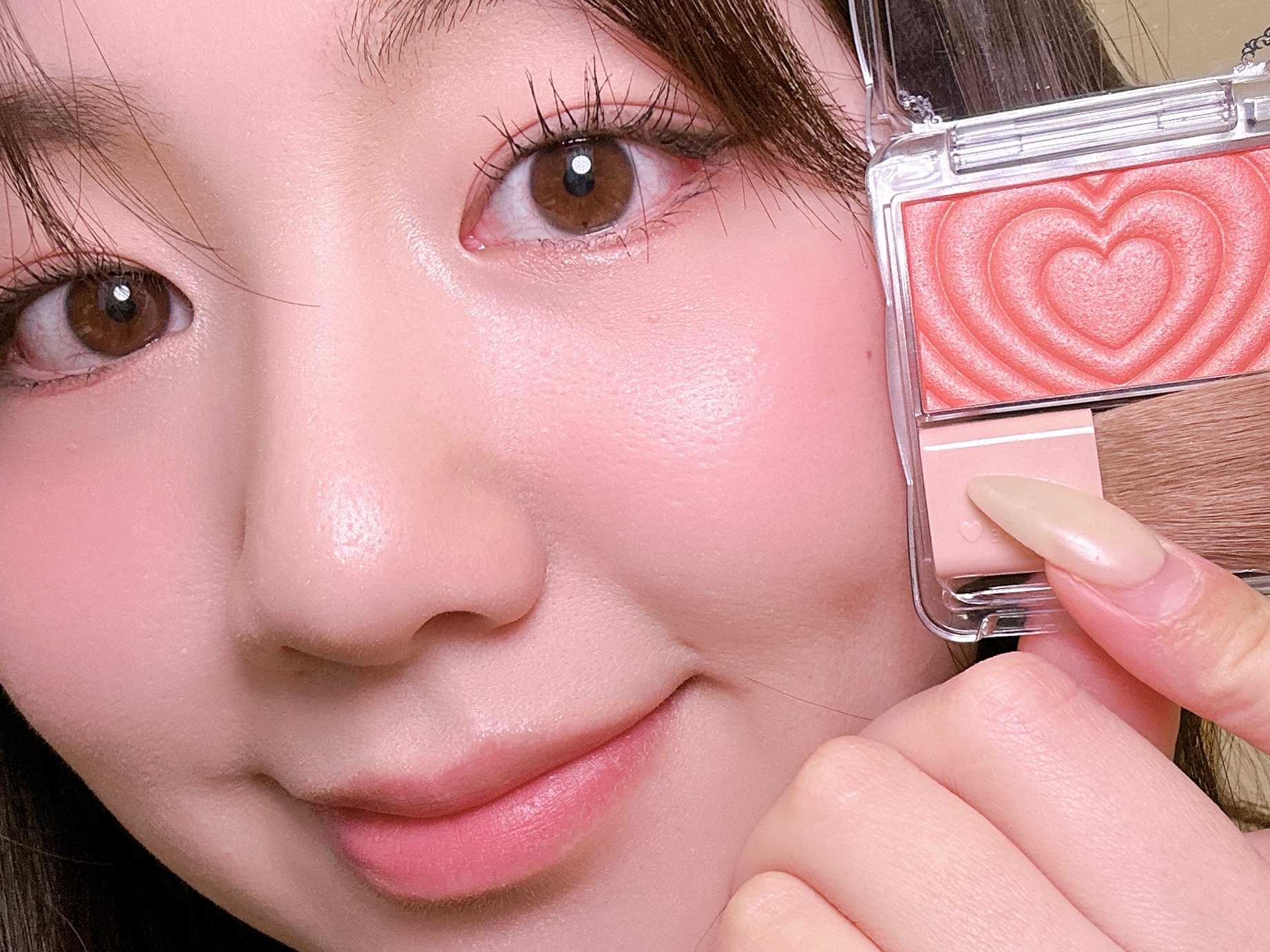 女性が愛らしいハート模様のチークを持ち、メイクをした笑顔のクローズアップ。