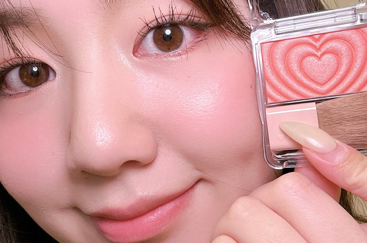 女性が愛らしいハート模様のチークを持ち、メイクをした笑顔のクローズアップ。