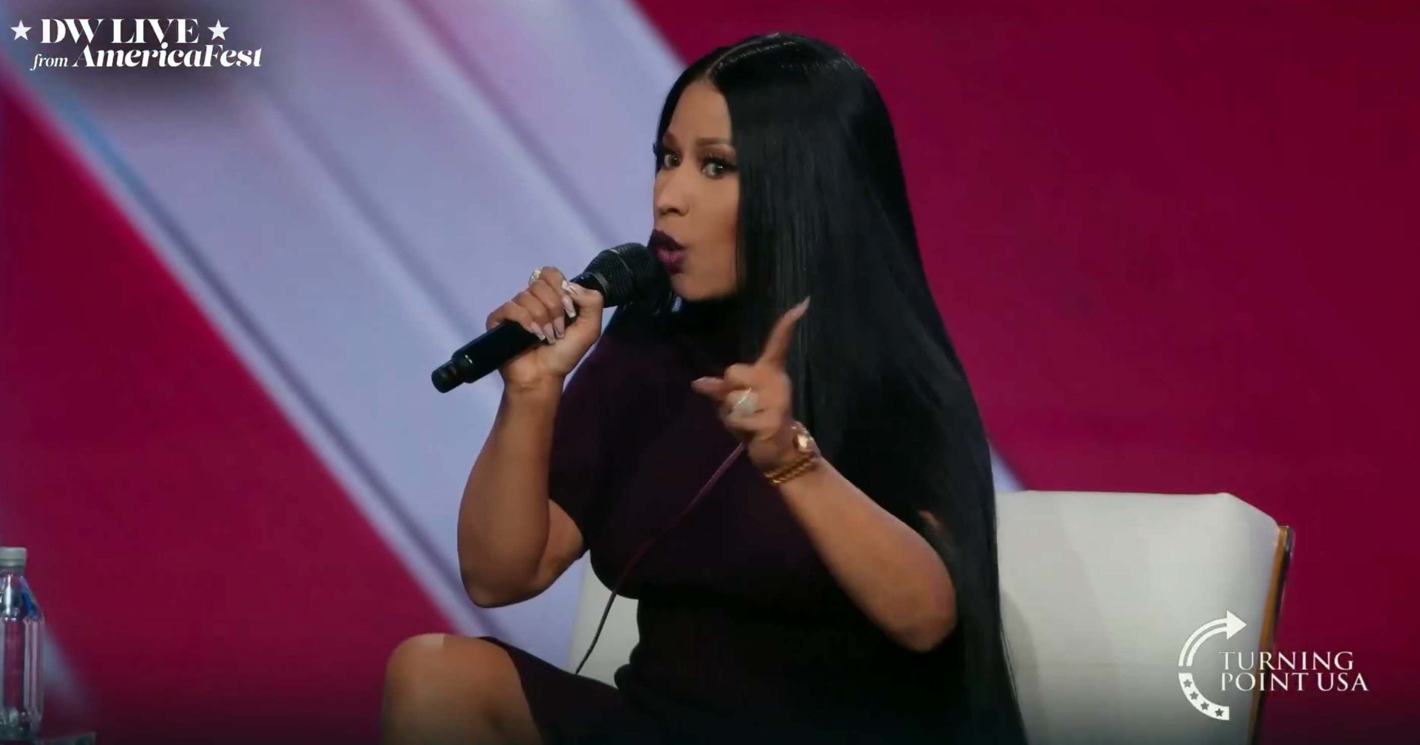 Person speaking passionately connected signifier with microphone, wearing sleek, modern outfit. Event branding disposable successful the background