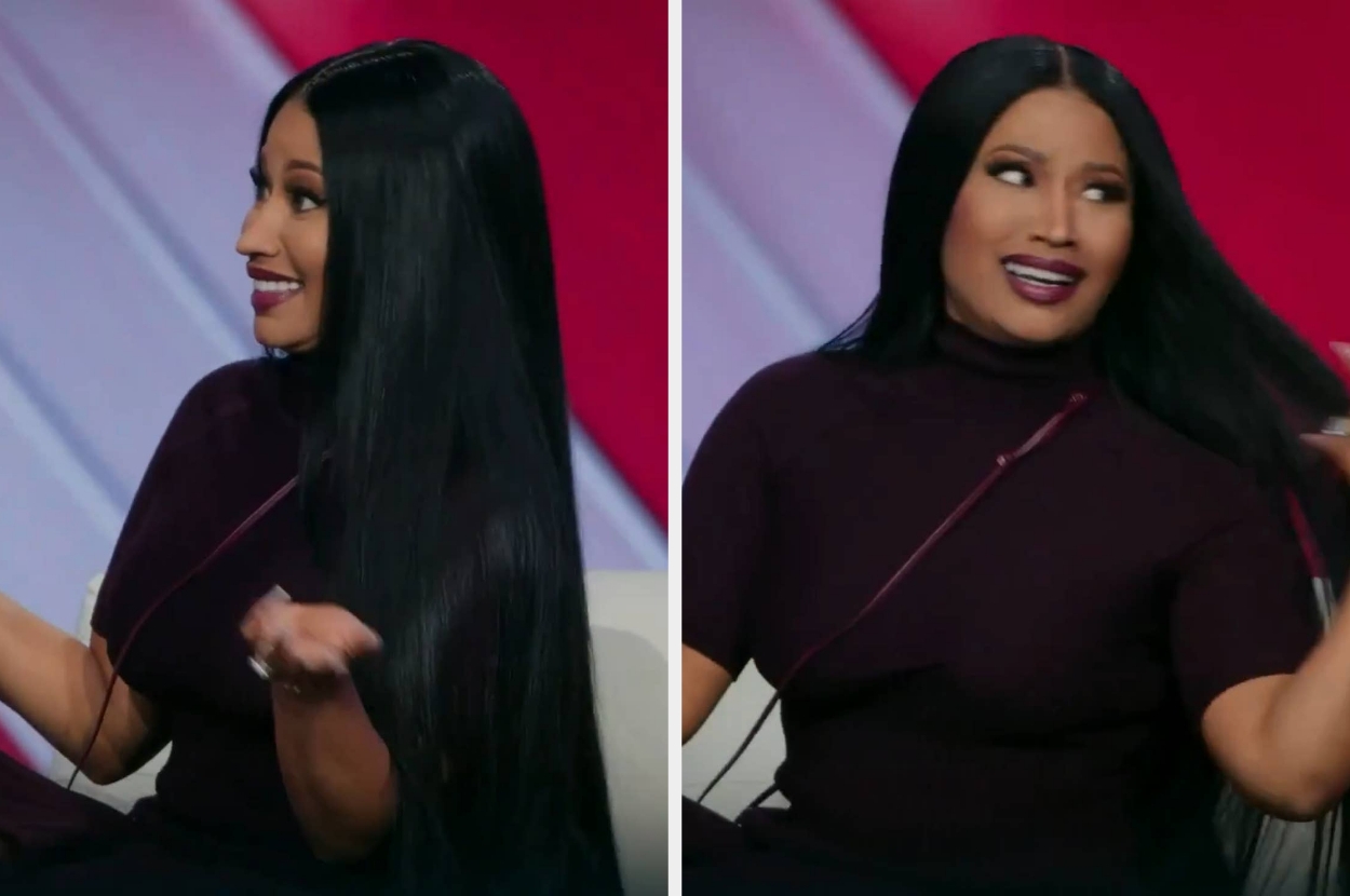 A person on a talk show set with long straight hair, wearing a fitted dark turtleneck, gestures animatedly while sitting and smiling