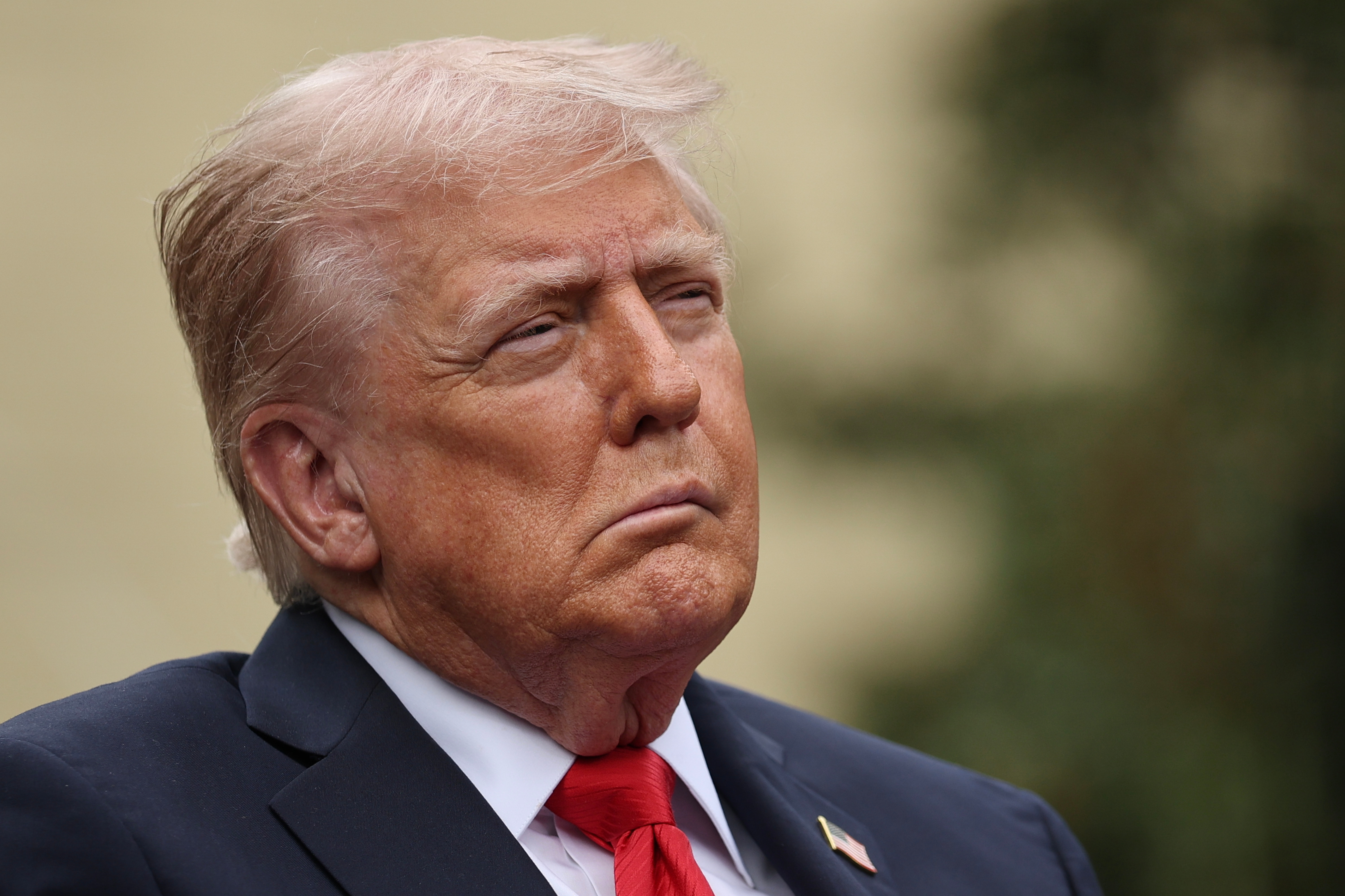 I don't cognize who this idiosyncratic is, but they're wearing a suit with a reddish tie, looking thoughtful outdoors