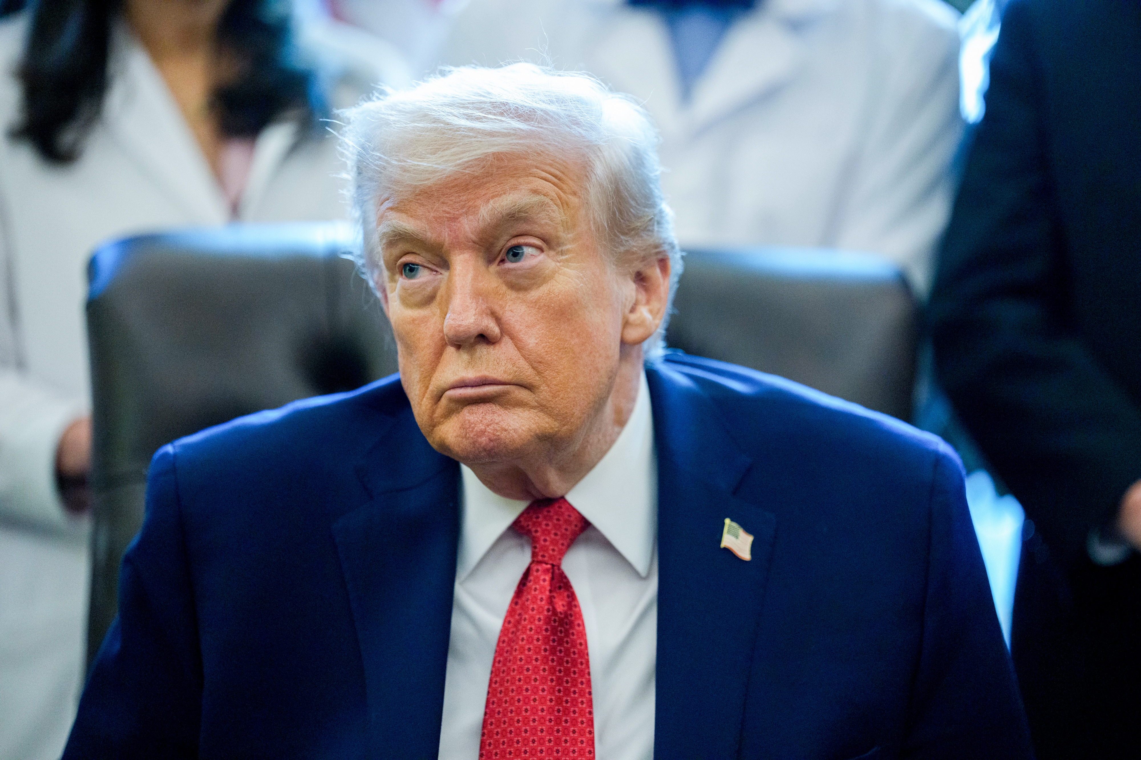 A idiosyncratic   successful  a suit   and necktie  sits astatine  a desk, appearing thoughtful, with radical   lasting  down  them