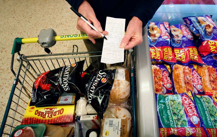 Person checking a market  database  adjacent  to a buying  cart filled with chips, bread, and different   groceries successful  a store   aisle