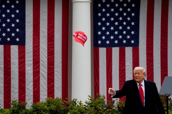 Person successful  a suit   gestures outdoors adjacent   U.S. flags, with a reddish  headdress  mid-air