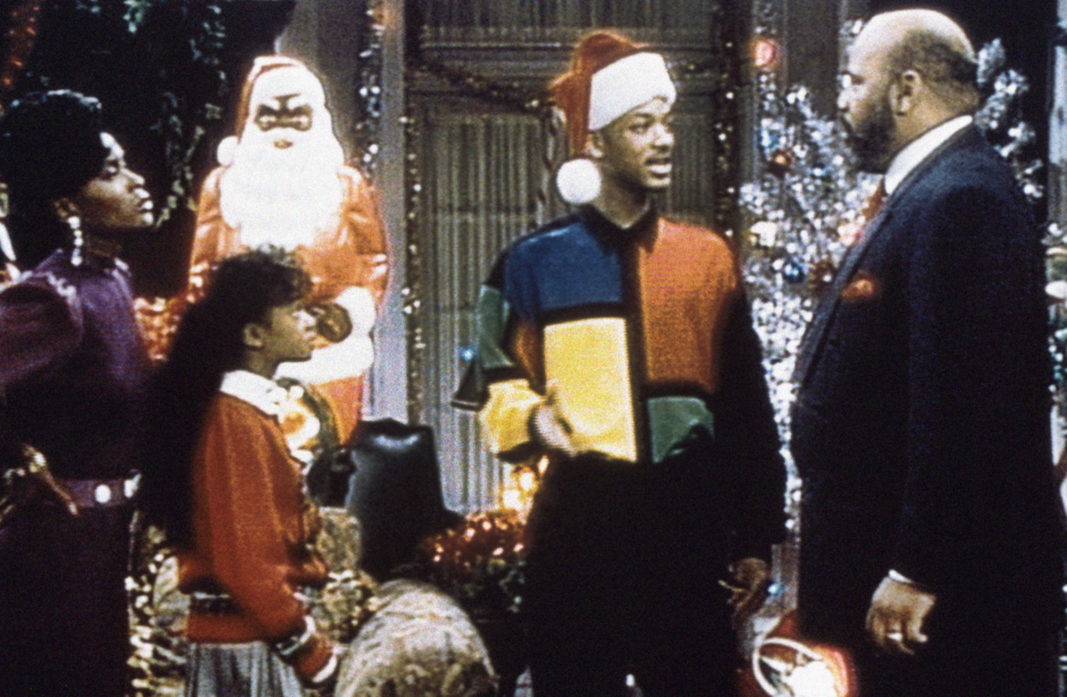 Family Christmas country from a TV amusement with characters successful conversation. One wears a color-block sweater and Santa hat, a festive histrion successful the background