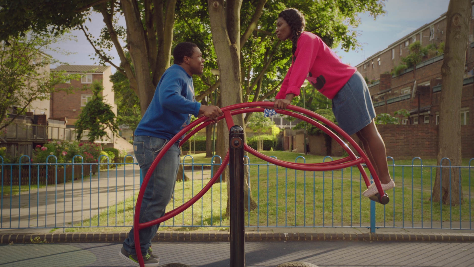 Two radical balancing connected a playground seesaw, smiling astatine each other. The mounting is an municipality parkland with benches and trees successful the background