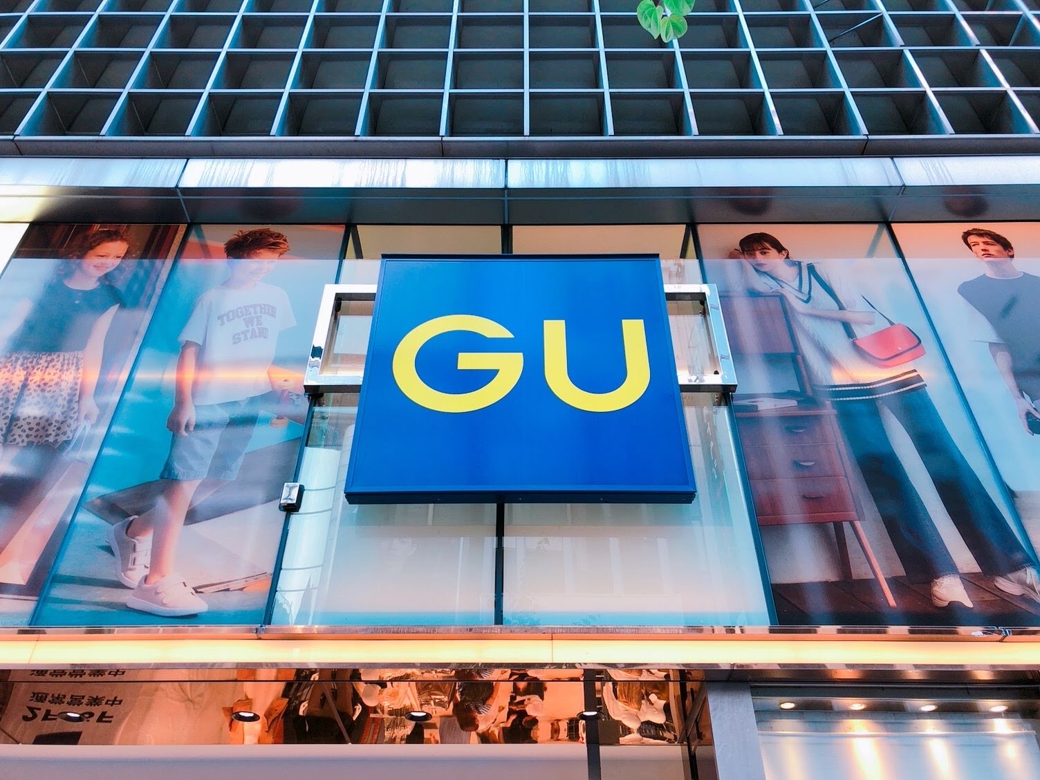 Storefront with a large "GU" sign on a building facade, featuring fashion displays on either side