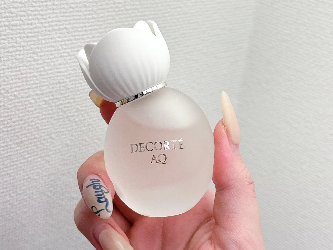 白い蓋が付いたデコルテAQの香水ボトルを手に持つ。ネイルデザインが特徴的。