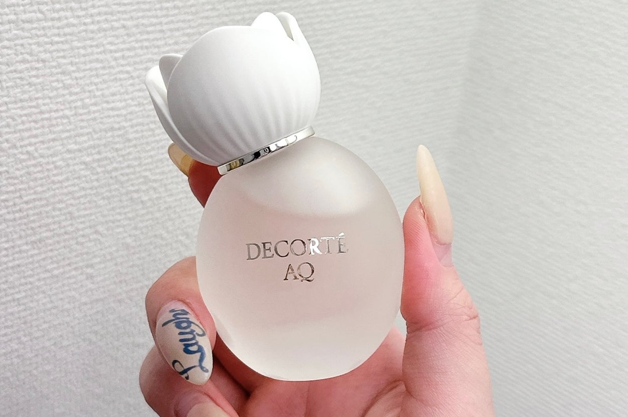 白い蓋が付いたデコルテAQの香水ボトルを手に持つ。ネイルデザインが特徴的。
