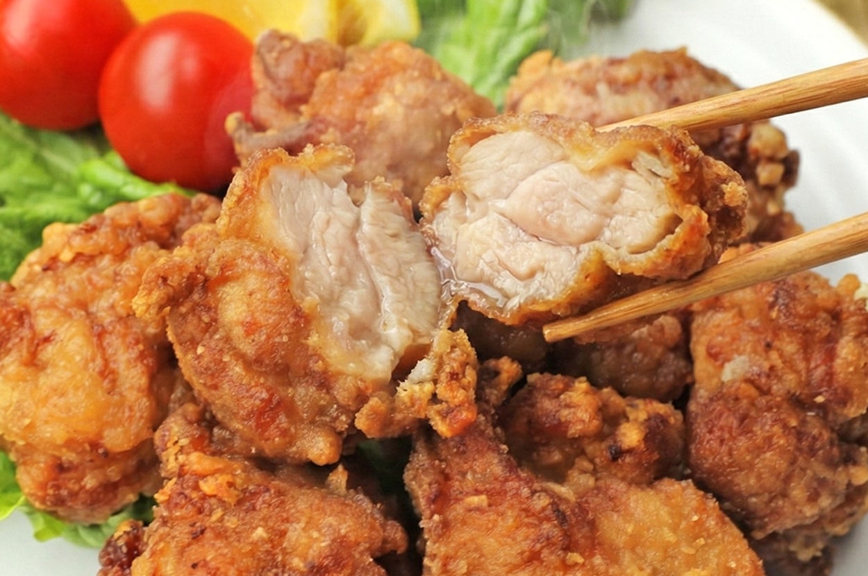 皿に盛られた唐揚げと付け合わせのレタス、トマト、レモン。箸で一つ持ち上げられている。