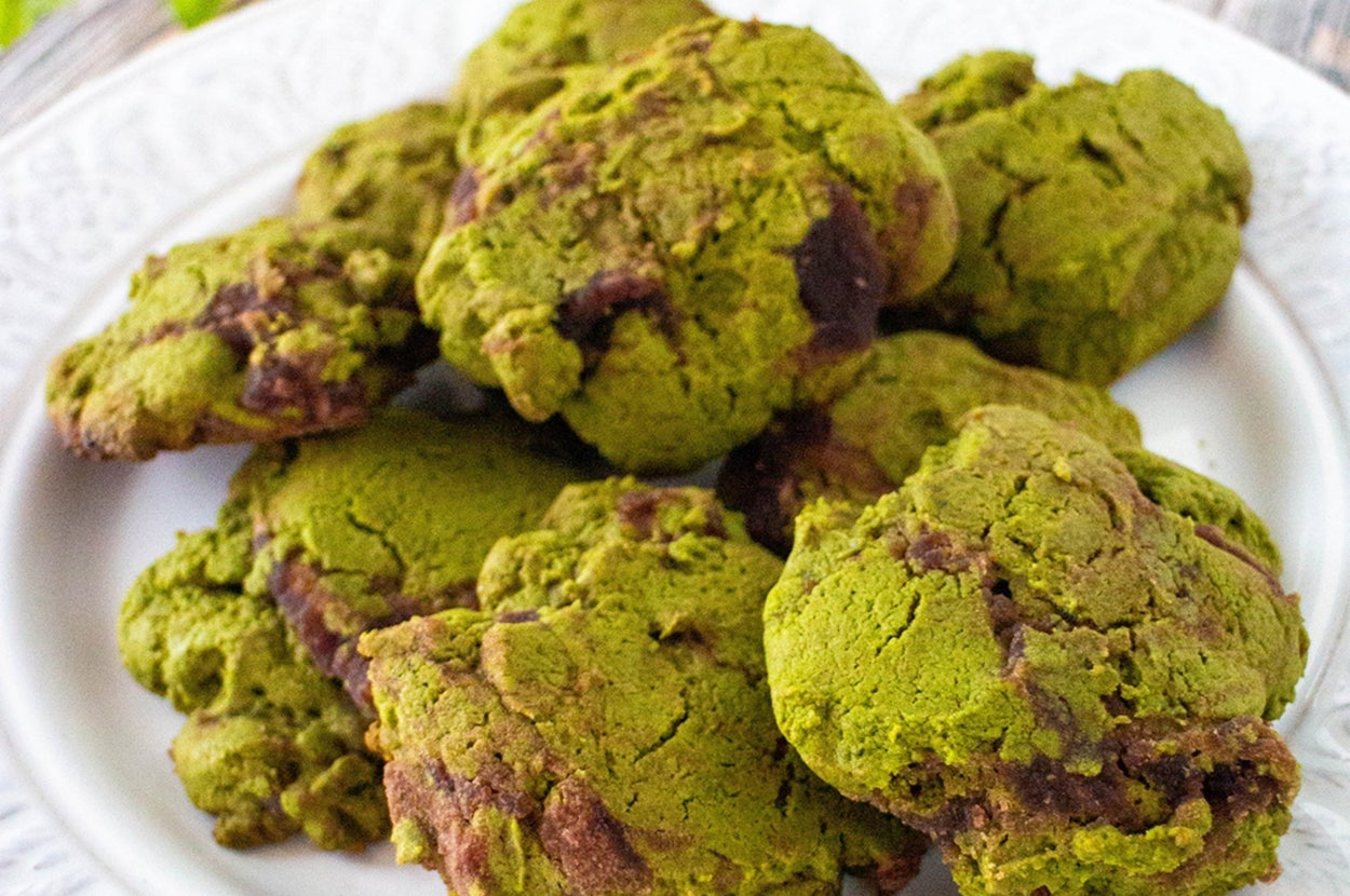 白い皿に盛られた緑のクッキー。背景に木のテーブルと葉が見える。