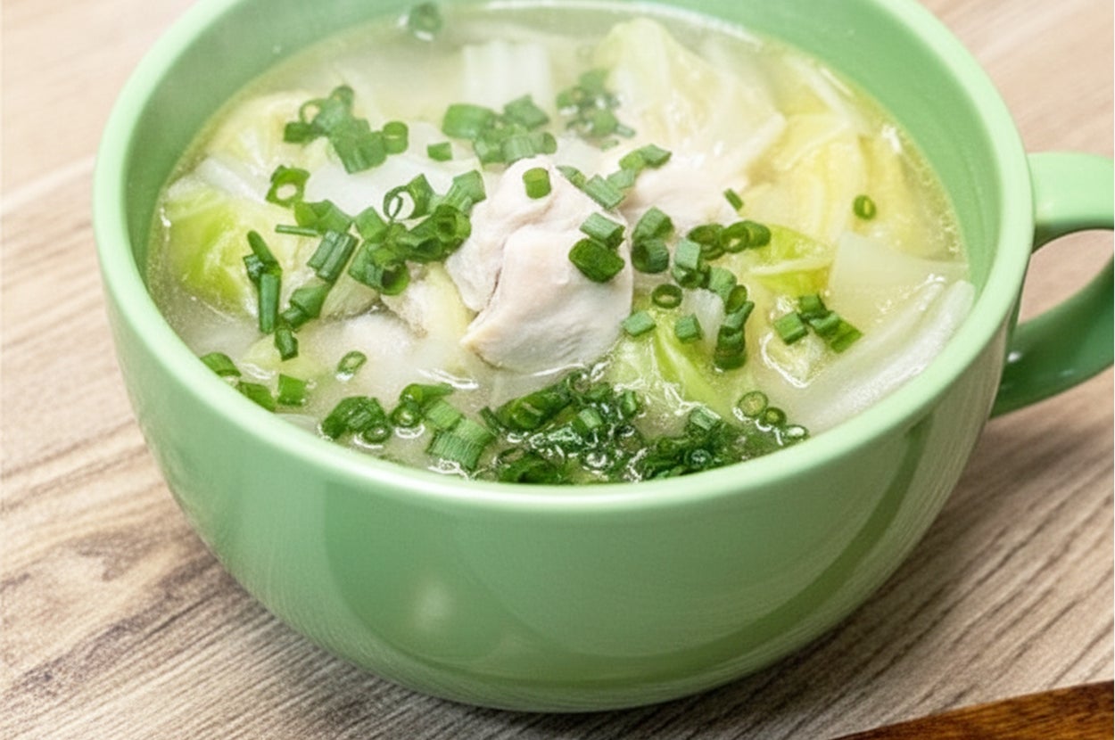緑色のボウルに入ったチキンと野菜のスープ。刻んだネギがトッピングされている。スプーンが横に置かれている。