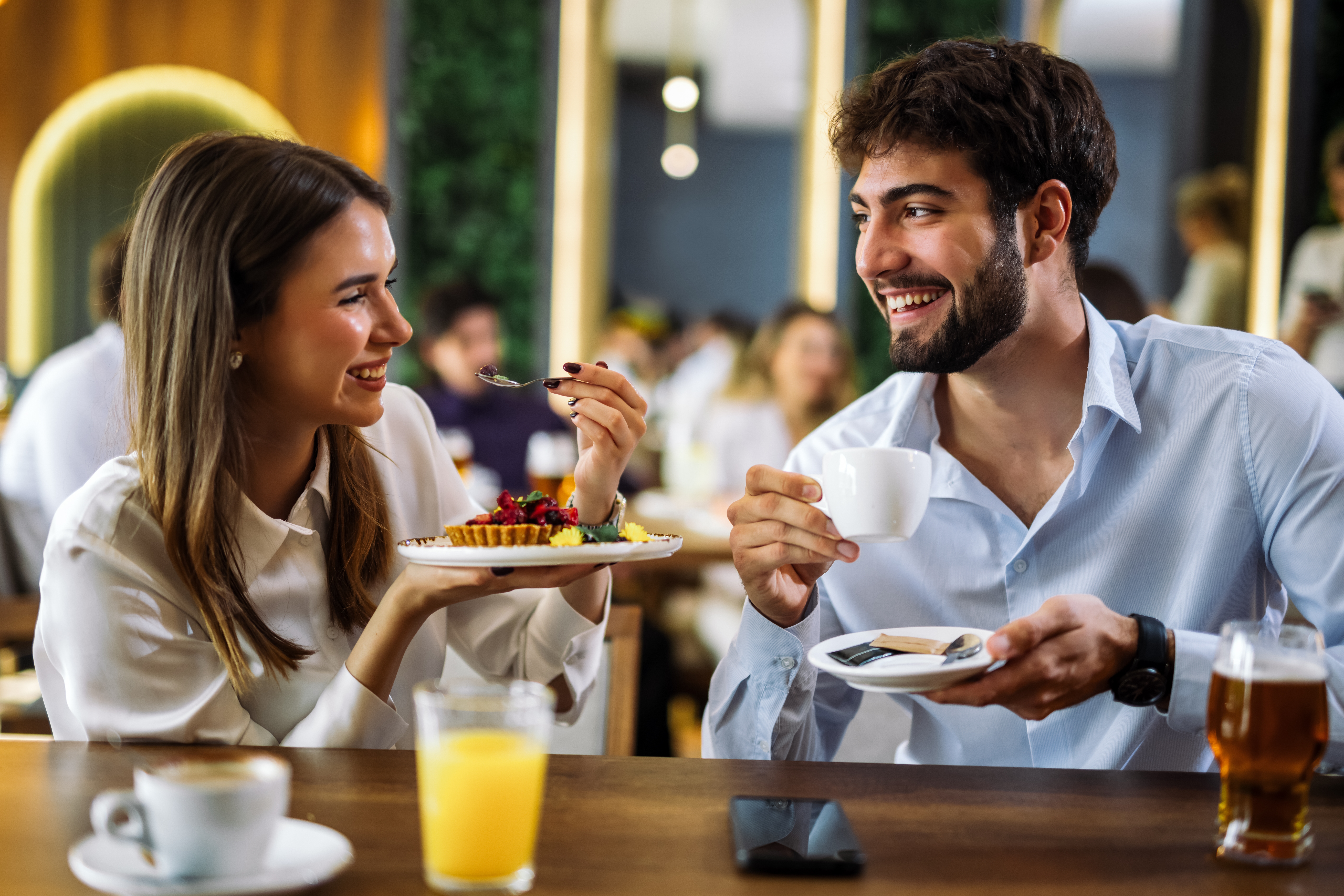To personer på en kafé, smiler og nyter kaffe og dessert sammen