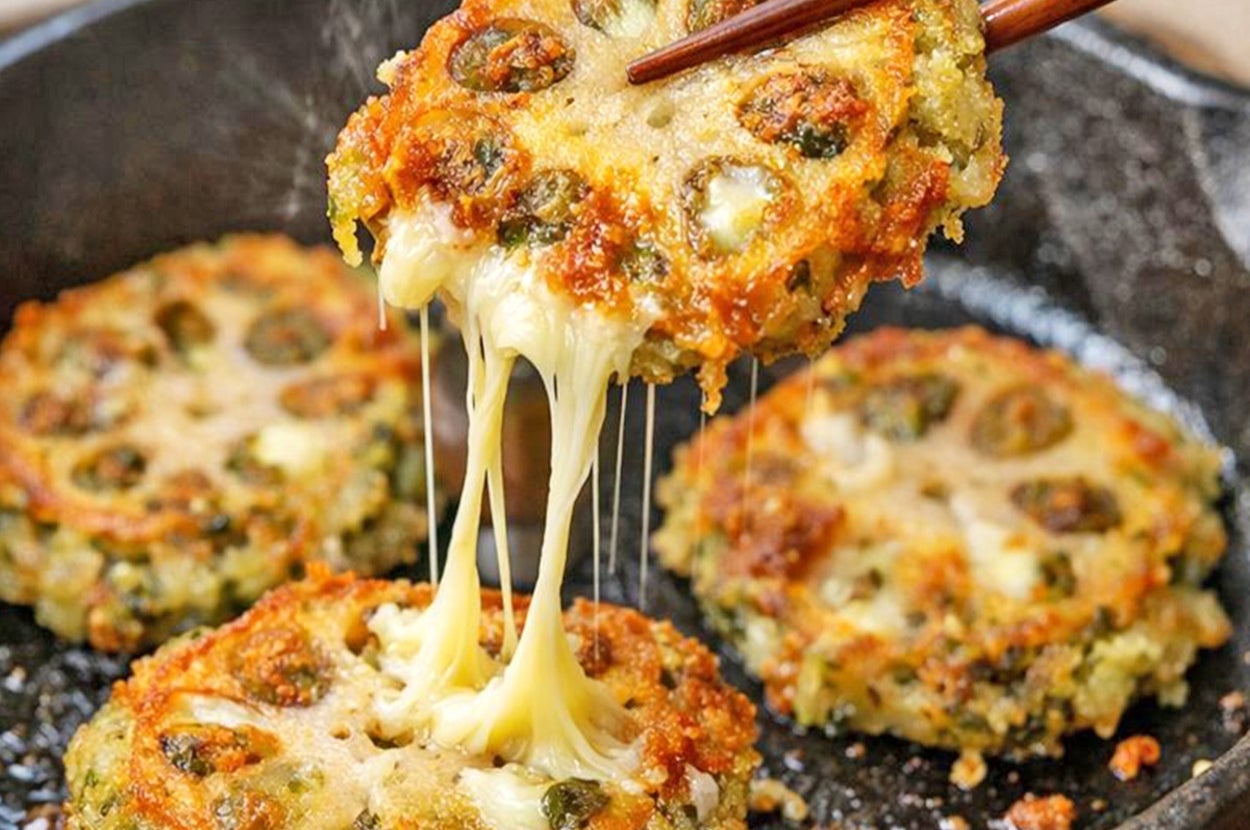 チーズがとろけるレンコンとチーズのはさみ焼きが鉄製のフライパンで調理され、箸で持ち上げられている。