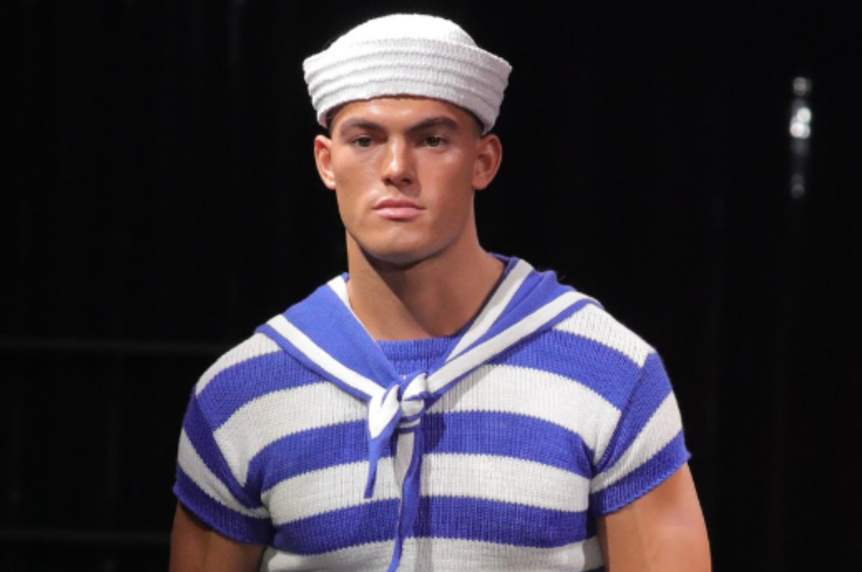 男性モデルがショーファッションで、水兵スタイルの半袖セーラーシャツと短パンを着てランウェイを歩いている。