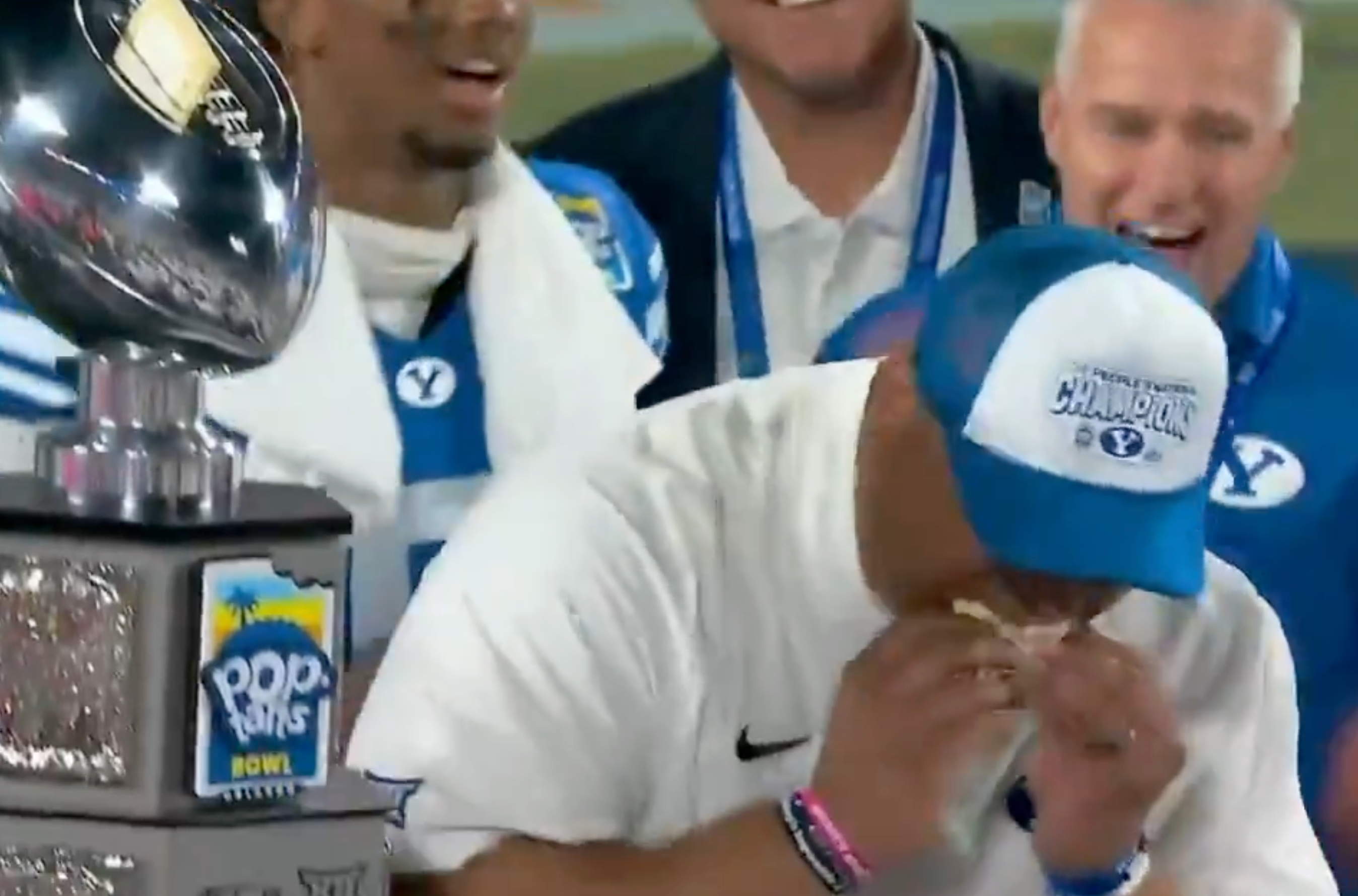 A coach, wearing a achromatic  garment  and bluish  cap, eagerly eats a Pop-Tart aft  winning a shot   game. A trophy is disposable   connected  a array  nearby