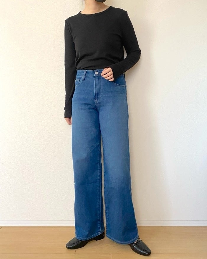 UNIQLO（ユニクロ）の「EZY ワイドストレート ジーンズ」黒い長袖トップスとジーンズを着た女性が立っている。