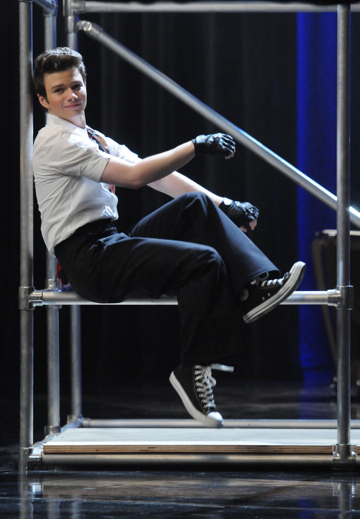 Chris Colfer successful  a achromatic  garment  and gloves, sitting playfully connected  a metallic  frame, wearing achromatic  pants and Converse sneakers. Performance setting