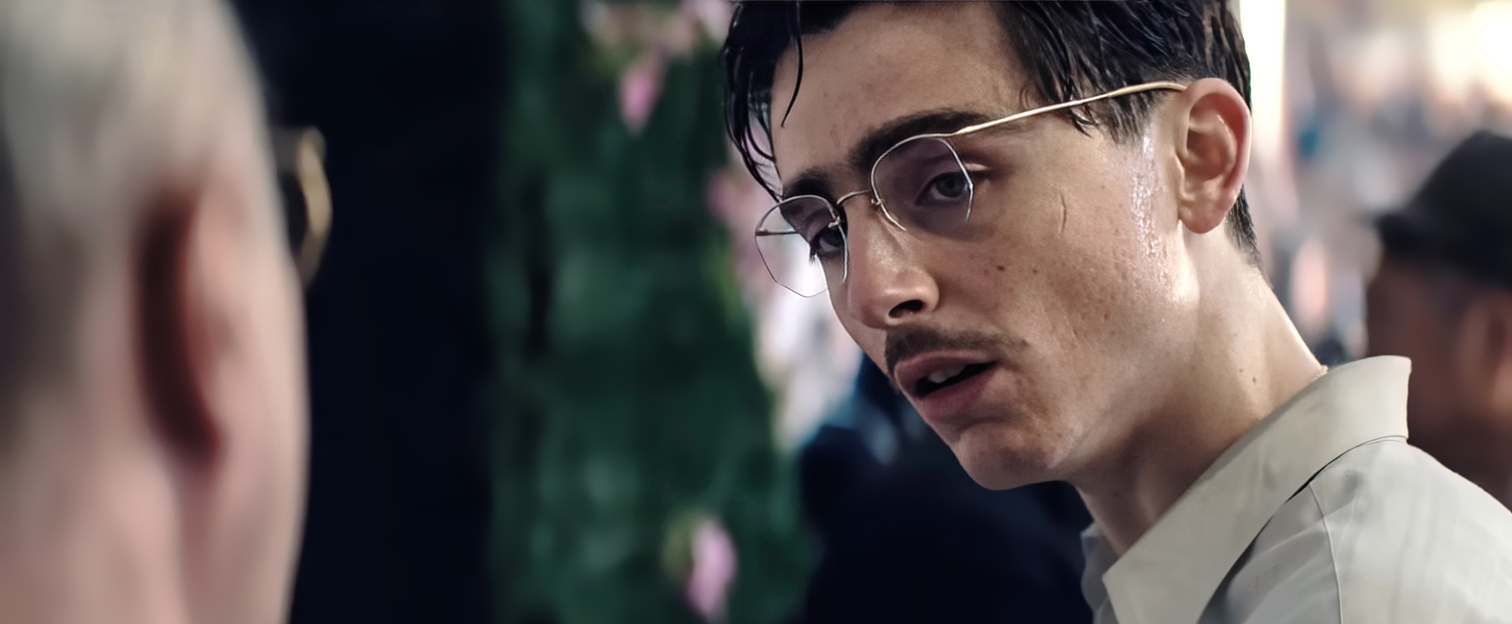 A idiosyncratic with glasses and a mustache looks intently astatine different person, suggesting a superior conversation