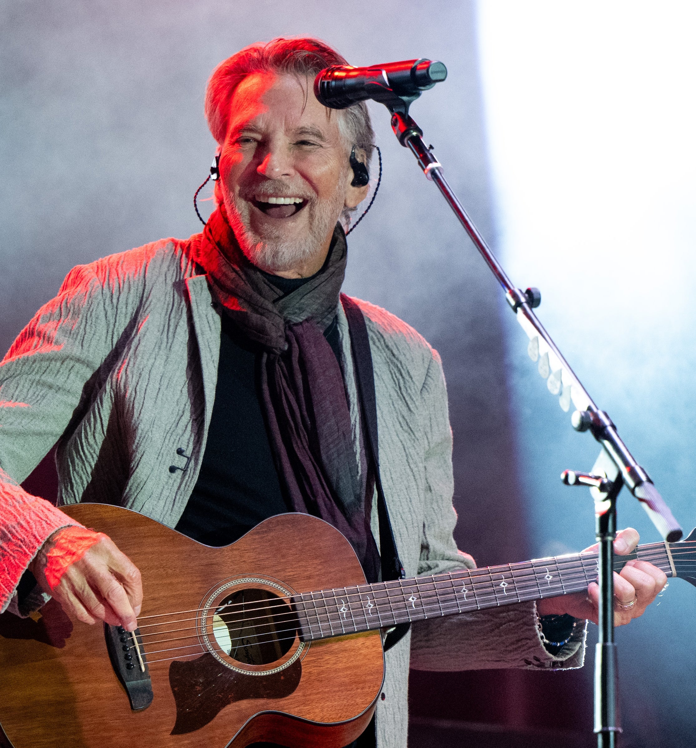 Musiker som opptrer på scenen med en gitar, iført en stripete jakke og skjerf, smiler til publikum