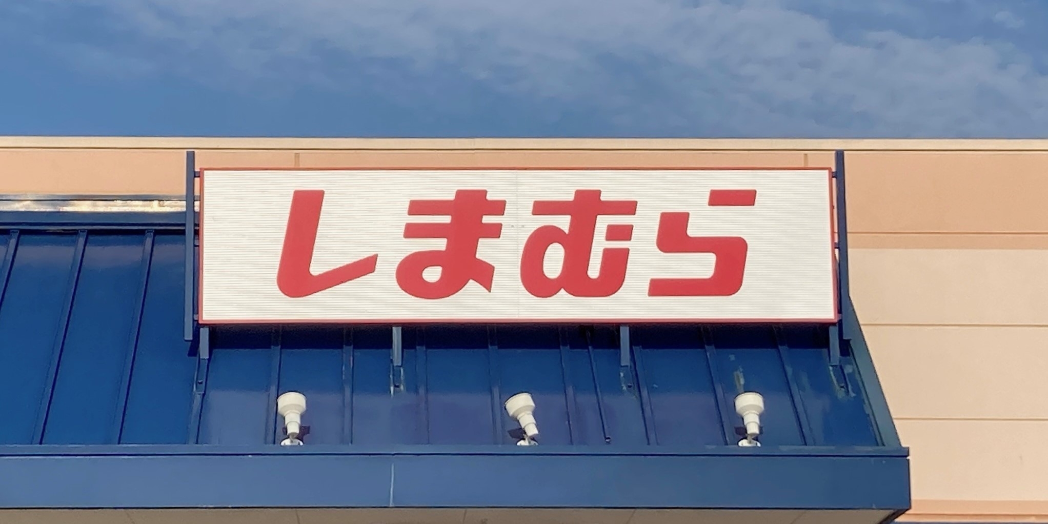 A store sign with red Japanese characters on a white background set against a building with a blue awning