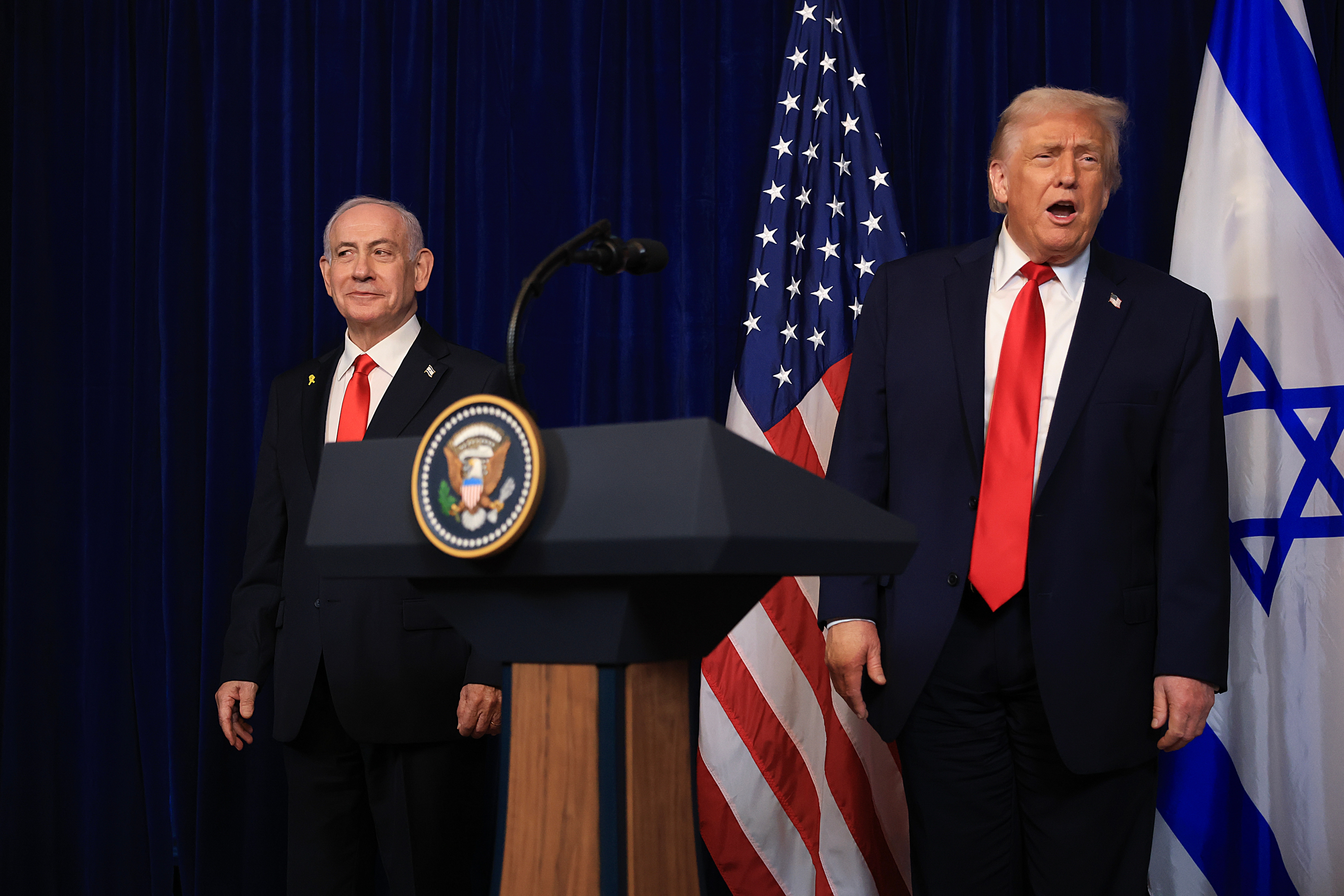 Two well-dressed men are astatine  a podium, with U.S. and Israeli flags successful  the background. One is speaking, some  deterioration  suits with reddish  ties
