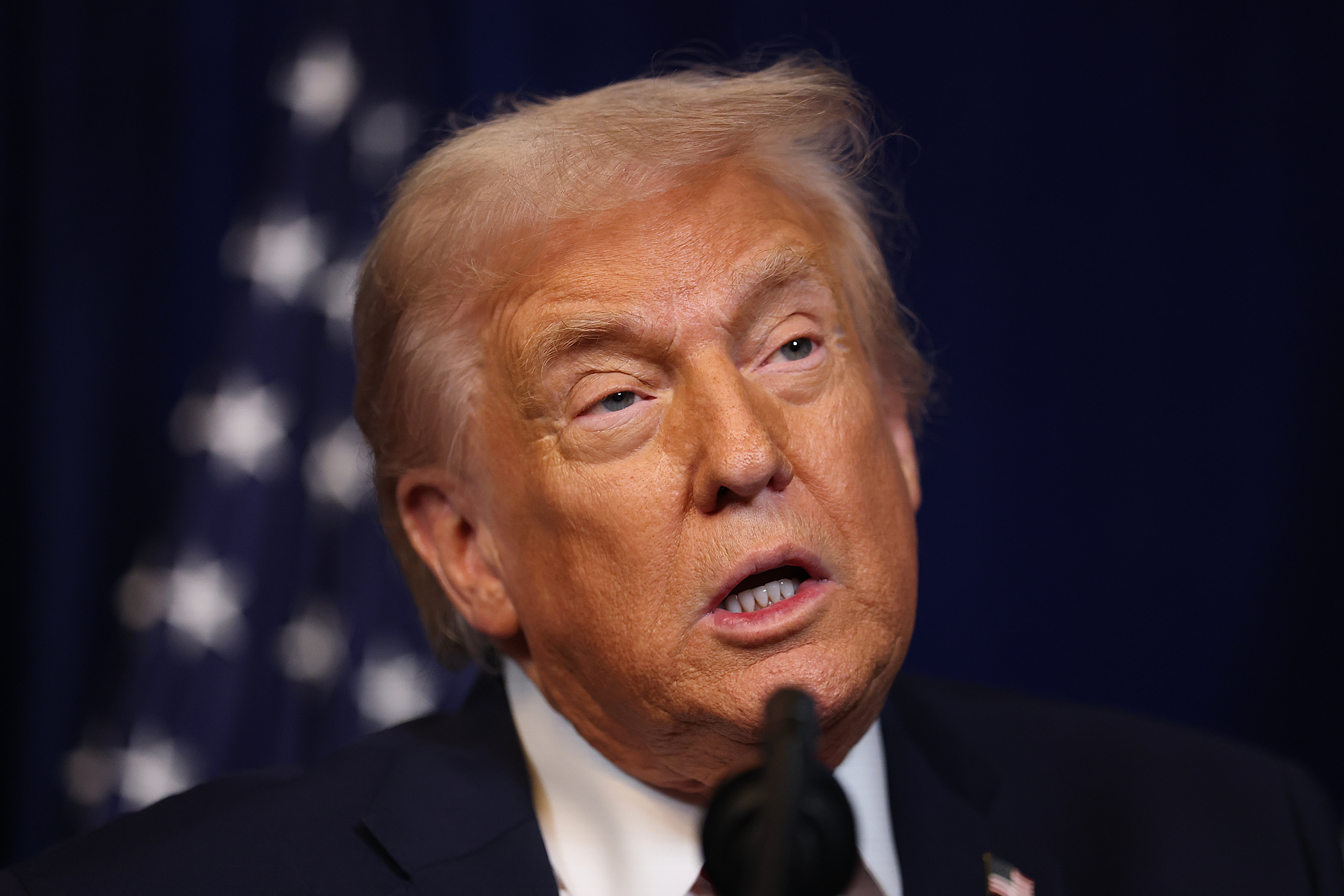 Man speaking astatine  an event, microphone visible. His look  is focused and intent