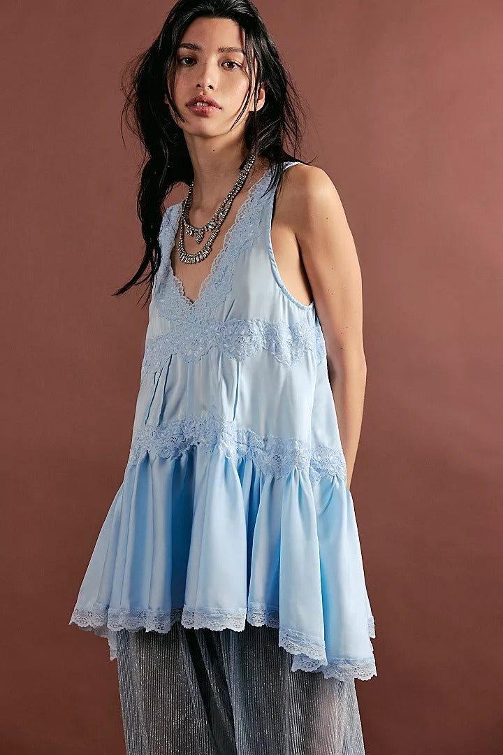 Model in flowy lace-trimmed tunic over sheer pants, posing against a plain backdrop, wearing layered necklaces