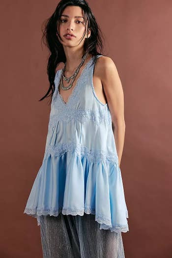 Model in flowy lace-trimmed tunic over sheer pants, posing against a plain backdrop, wearing layered necklaces