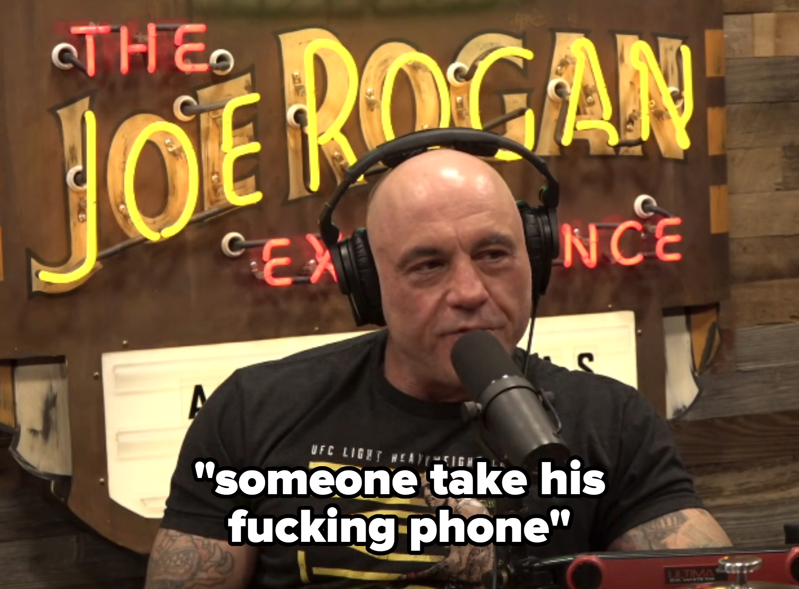 Person i en t-skjorte med hodetelefoner som snakker i en mikrofon under et podcastopptak. Opplyst skilt i bakgrunnen