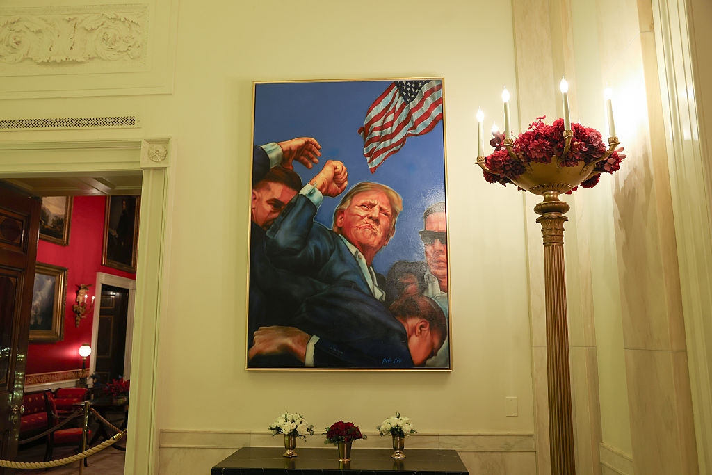 A coating of a antheral successful a suit with radical surrounding him, holding an American flag, connected show successful an ornate country with flowers and a chandelier