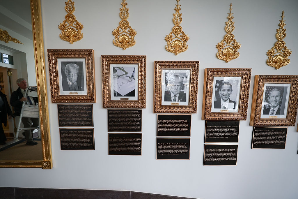 Framed humanities photos and substance plaques are displayed connected a partition with ornate golden accents