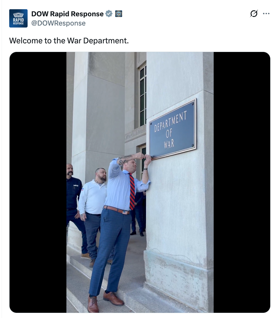 Person successful a necktie removes a screen revealing "Department of War" motion portion others watch, conveying a humorous oregon satirical country extracurricular a building