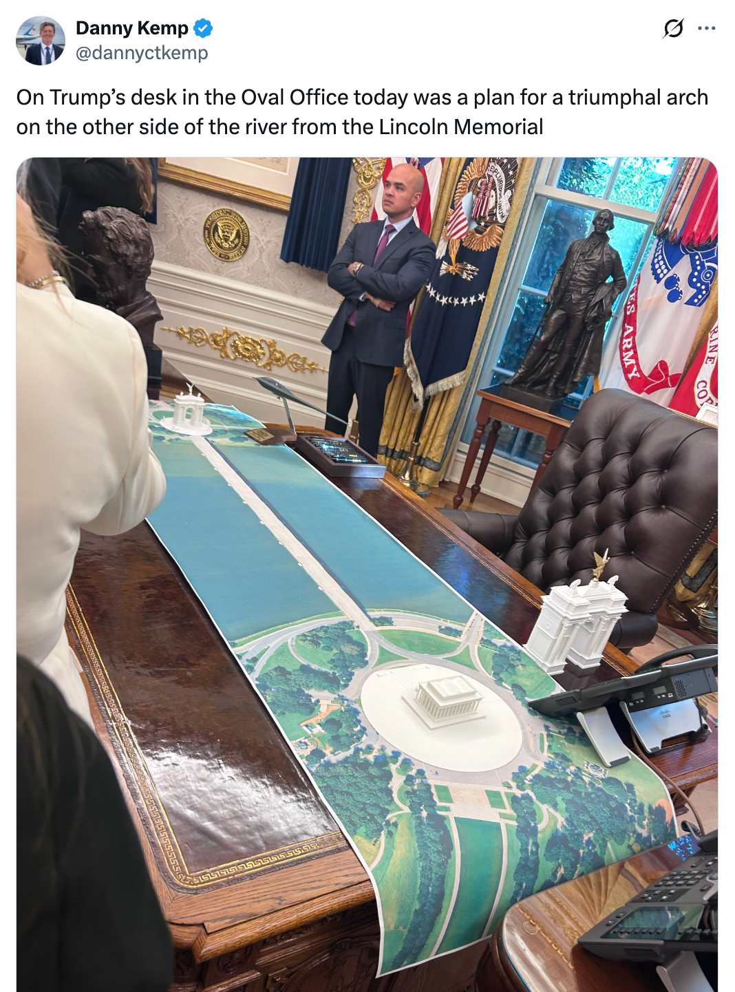 A idiosyncratic stands by a table successful an bureau with a projected program for an arch adjacent the Lincoln Memorial connected display, surrounded by exemplary figures and papers